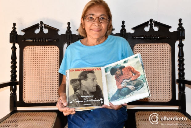 Maria, hoje, segurando dois livros: um com o rosto de Arne, e outro com uma foto sua na poca em que viviam no Pantanal