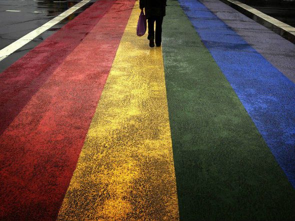 Pessoa caminha em rua pintada com as cores da bandeira gay